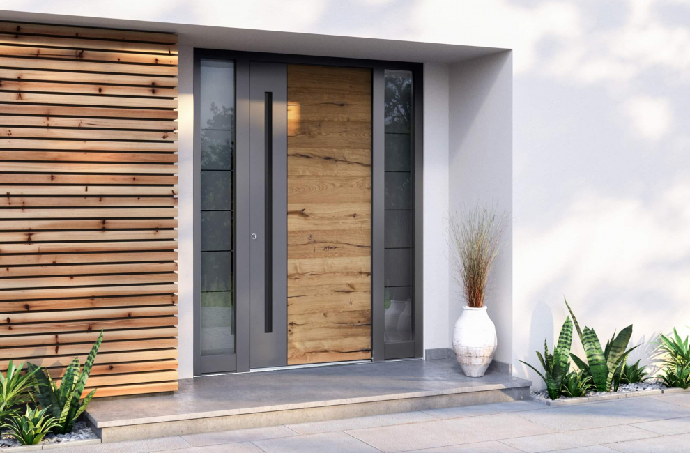 Moderna aluminijasta vhodna vrata, odeta v leseni dekor, pred vhodom pa je rastlinska dekoracija.