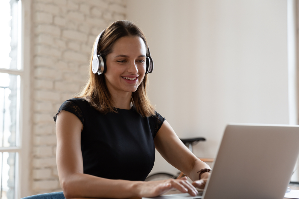 Eine Frau mit Kopfhörern sitzt an einem Schreibtisch und tippt auf einem Computer.