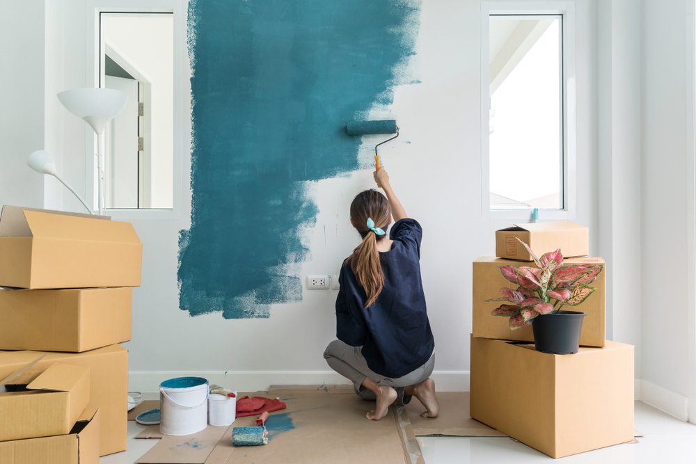 Eine Frau streicht mit einer Walze die Wand in einem neuen Zuhause.