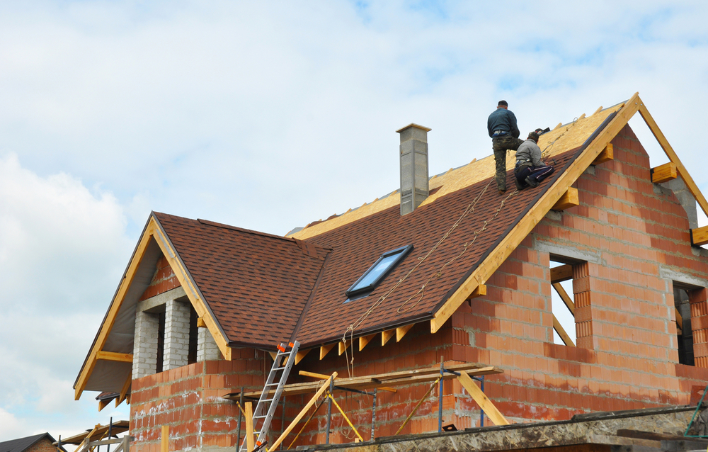 Hausbau - Baumeister legen Ziegel auf das Dach. 