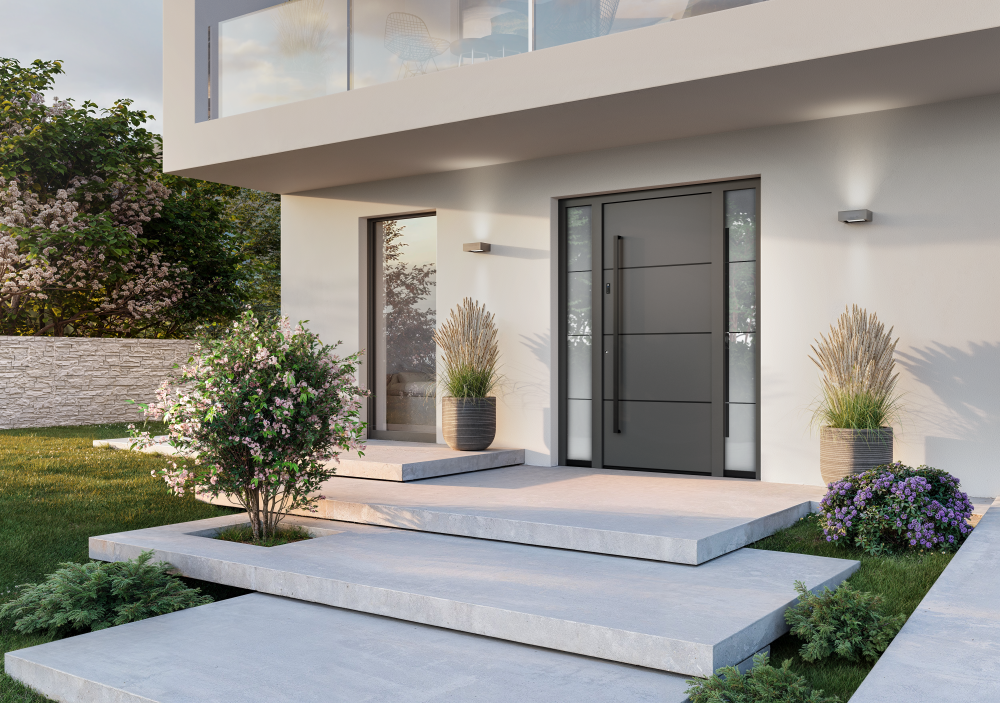 Svetla fasada hiše z velikim oknom, sivimi vhodnimi vrati in cvetjem pred hišo.